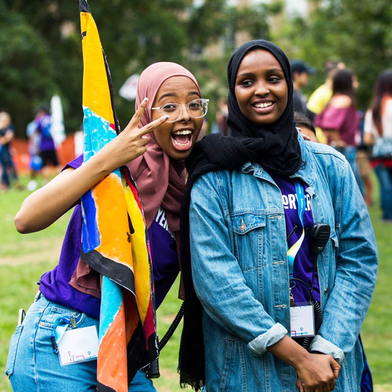 Two Black students in hijabs laugh while posing at an event in the TMU Quad.