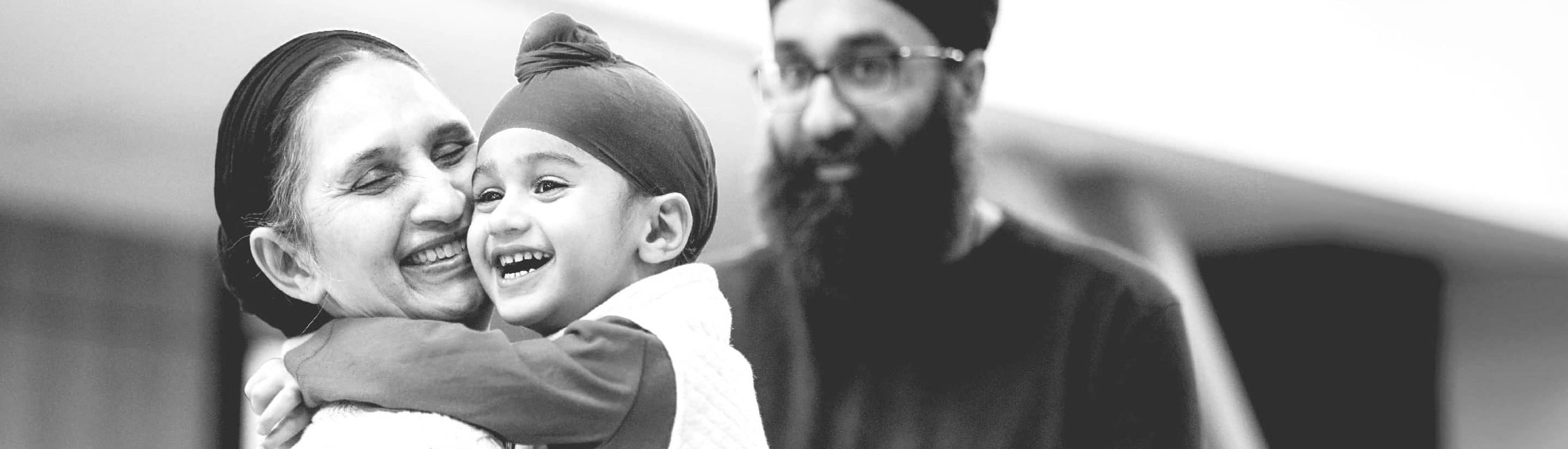 A child hugging his grandmother as his father watches proudly