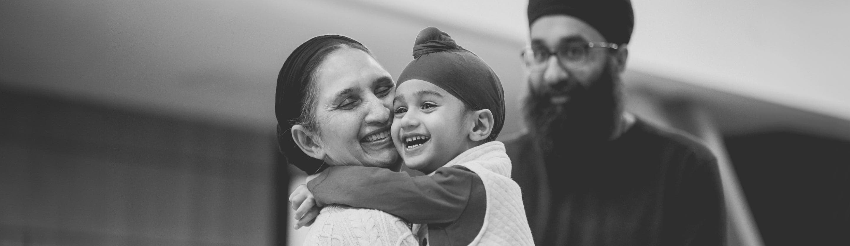 A child hugging his grandmother as his father watches proudly