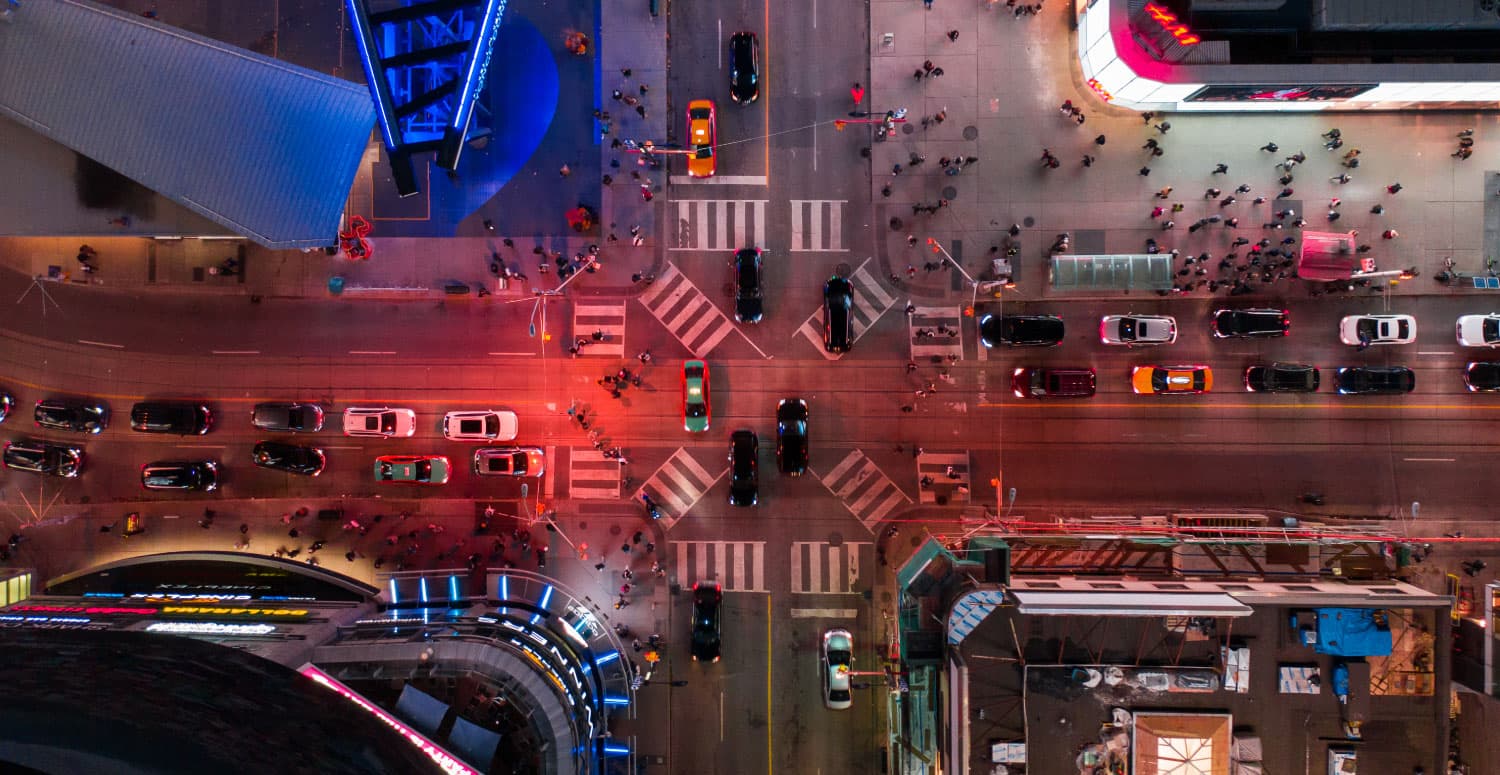 A bustling downtown intersection at night illuminated by vibrant blue and red lighting.