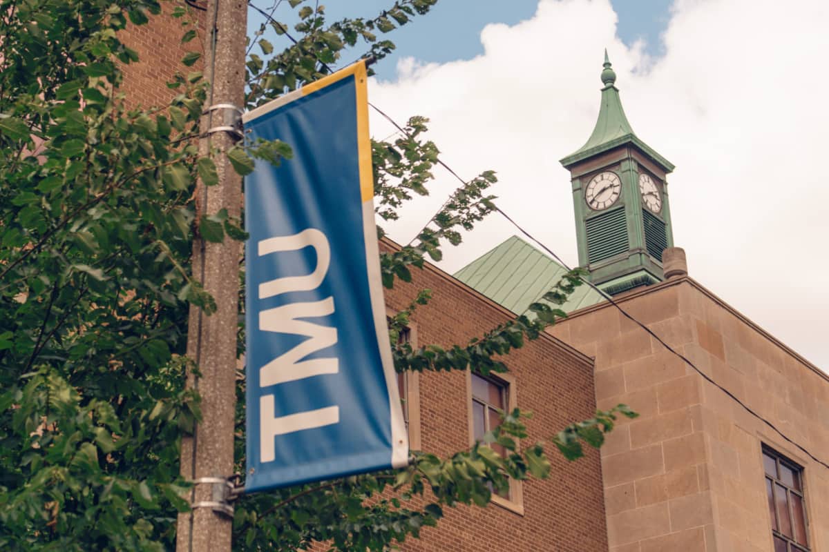 Toronto Metropolitan University street flag in front of a campus building against a backdrop of blue sky, representing the vibrant campus atmosphere.