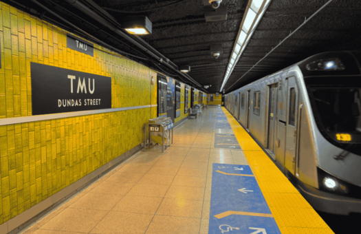 TMU subway platform with a train stopped along the platform and yellow tiled station walls.