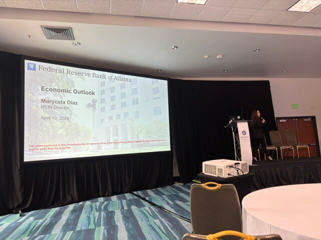 Speaker Marycela Diaz at the podium with a large presentation screen displaying "Federal Reserve Bank of Atlanta: Economic Outlook."