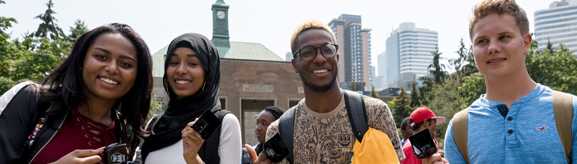 Four students (two women and two men) stand smiling broadly in the Kerr Hall Quad with the clocktower in the background.