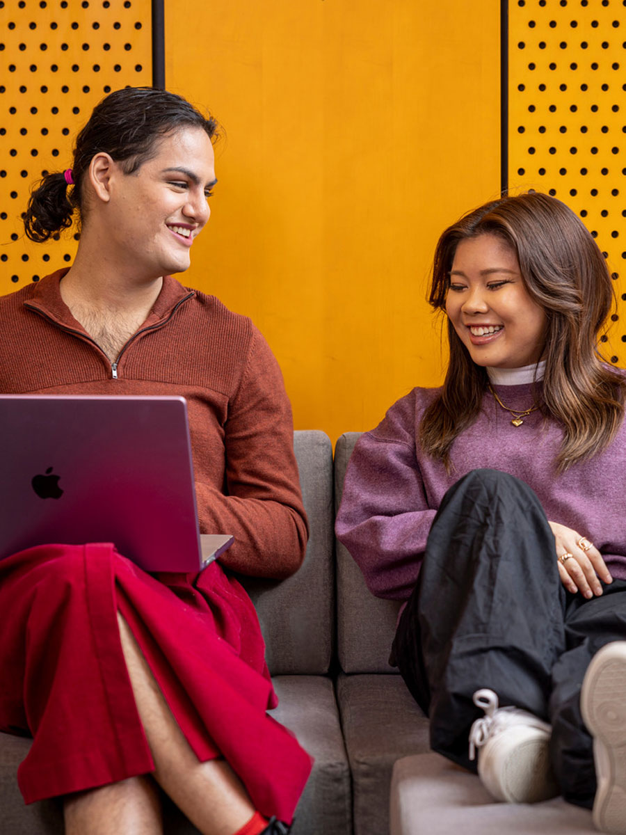 Two seated students smiling while looking at a laptop