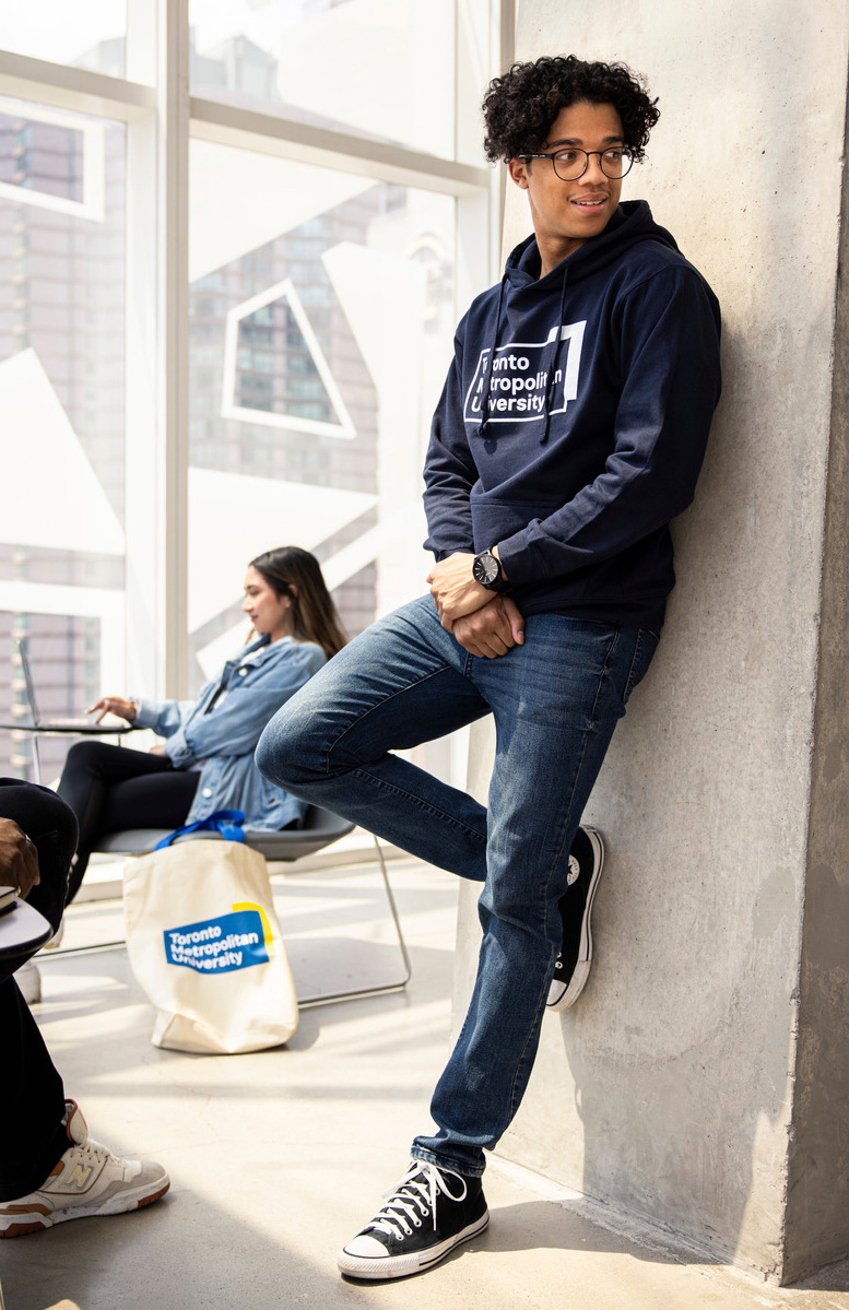 Student wearing a Toronto Metropolitan University (TMU) leaning against a concrete wall
