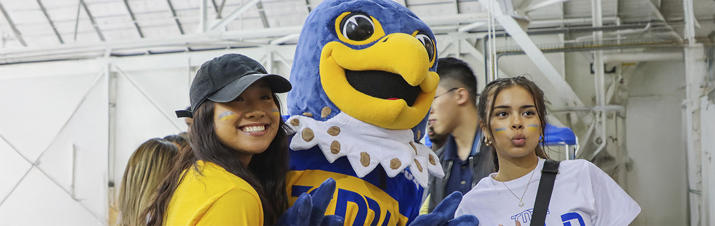 2 students smiling with our TMU mascot, Frankie B. Bold, at the Mattamy Athletic Centre.