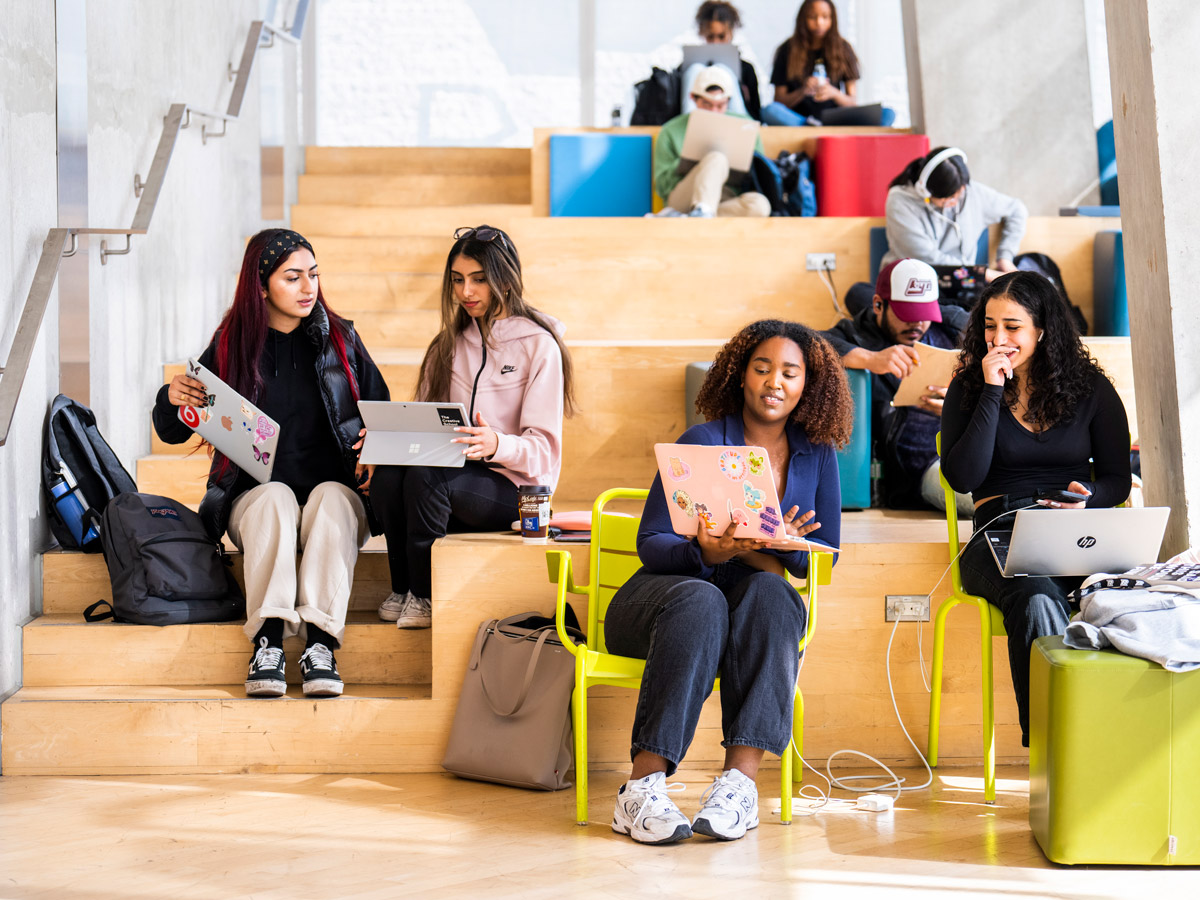 Students working and chatting on the colourful and bright stairs of the SLC Beach floor.