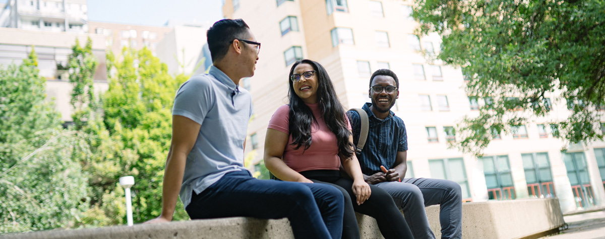 Three students sitting together in the quad, looking at each other and smiling