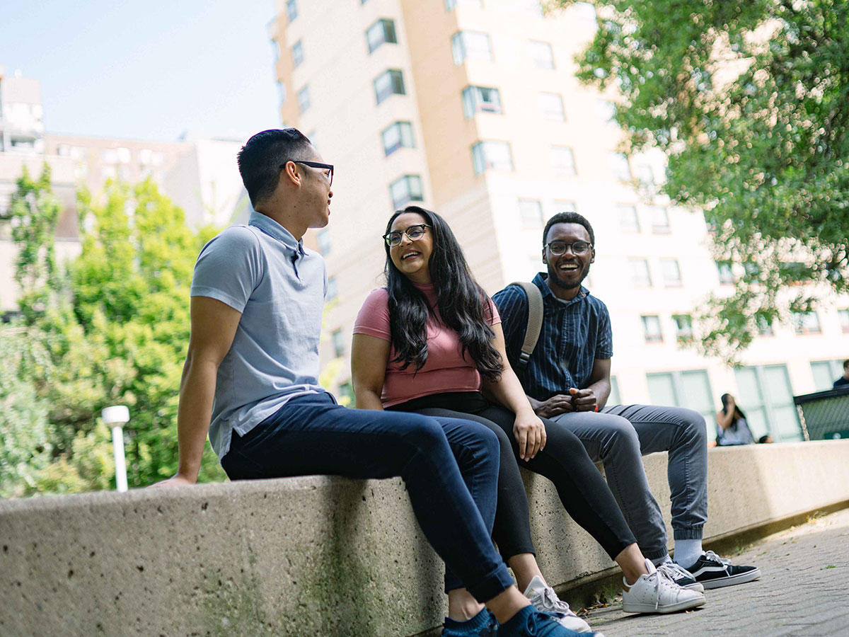 Three students sitting together in the quad, looking at each other and smiling