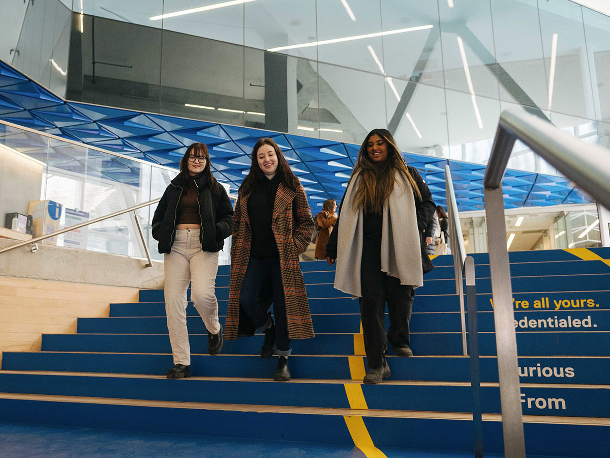 Three students walking down a flight of stairs inside of the Student Learning Centre (SLC).