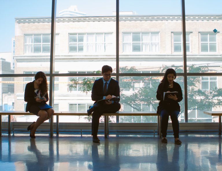 Students on a bench, in business attire in the Enginering building hall way.