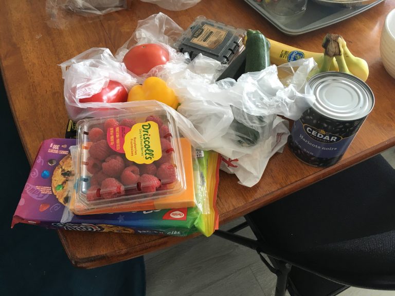 Grocery items on a table, raspberries, coockies, canned food, banana, cucumber and more.