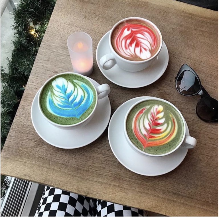 Three cups of colourful coffee art on a table with sunglasses