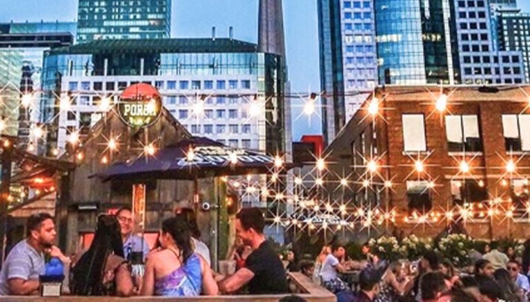 The Porch patio space with a lot of people in groups sitting on tables on a summer evening.