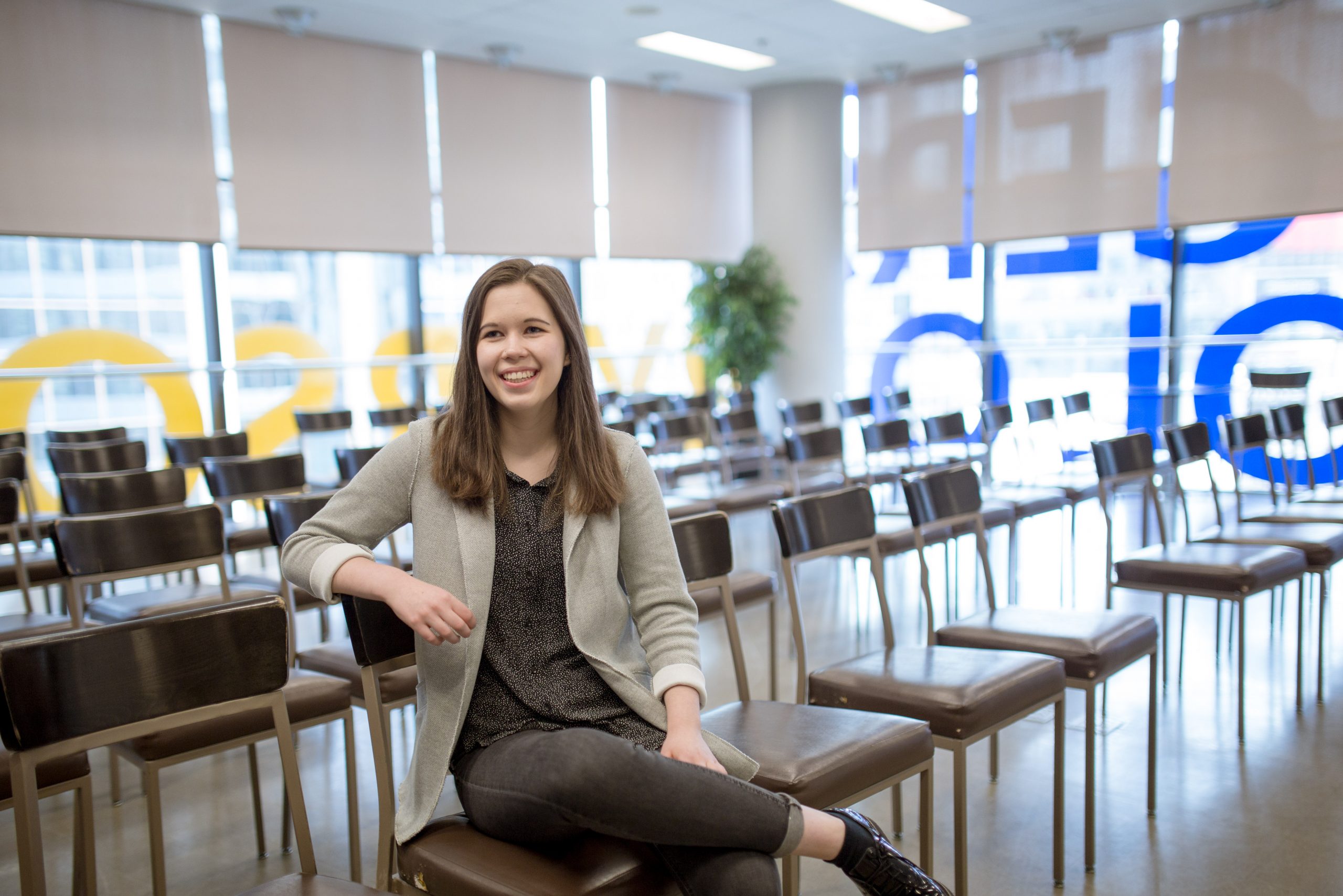 Emma sitting in a room full of empty chairs inside the Ted Rogers School of Management building.