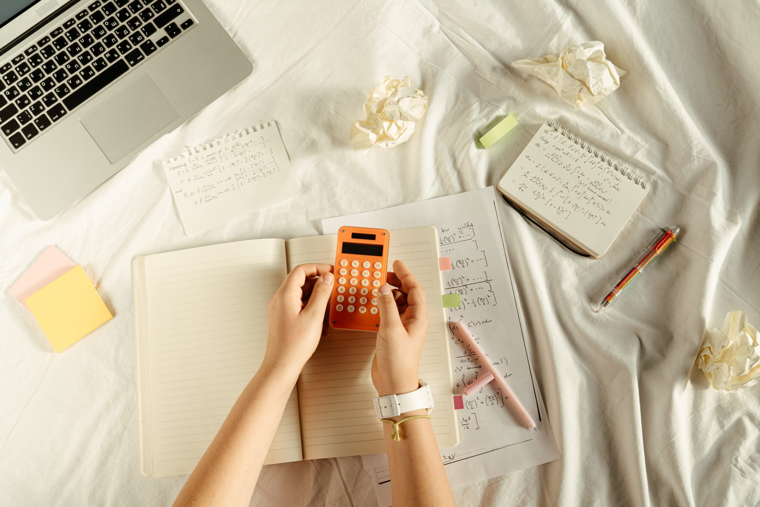Student using calculator to complete math homework while sitting on bed.