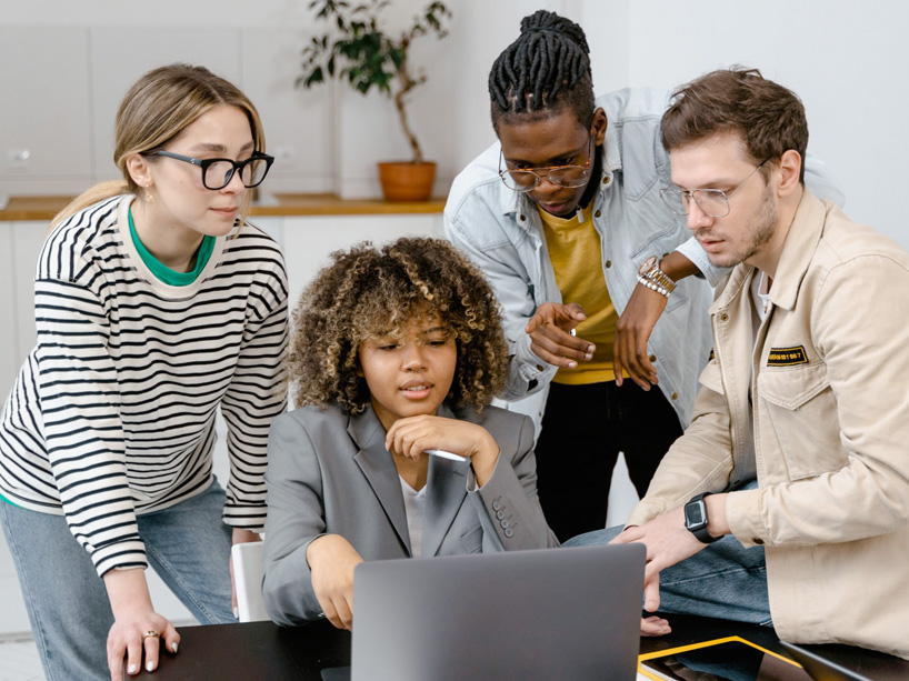 Four students hovering over a laptop while they study