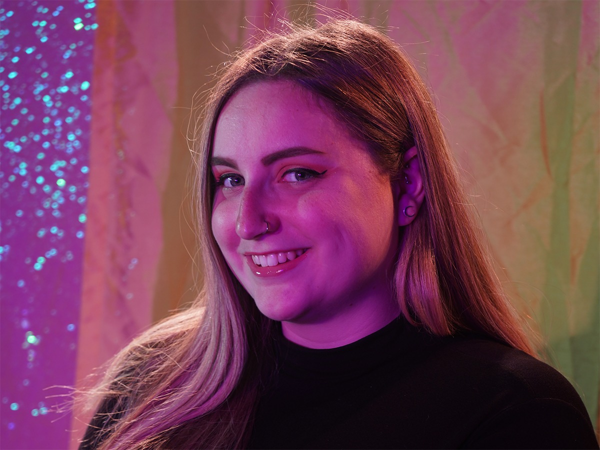 Carly sitting in front of a yellow and purple backdrop for a photo shoot