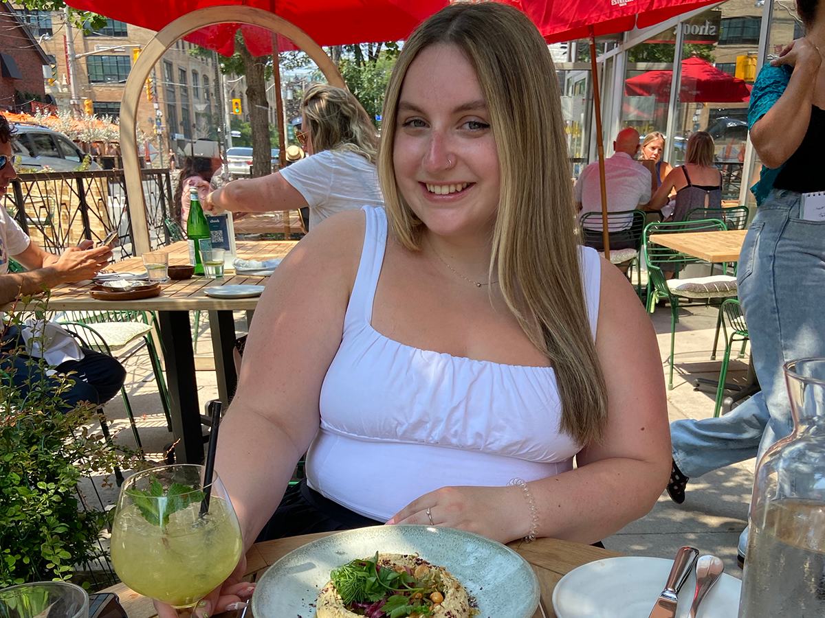 Carly sitting on the patio at Shook Kitchen with a plate of hummus