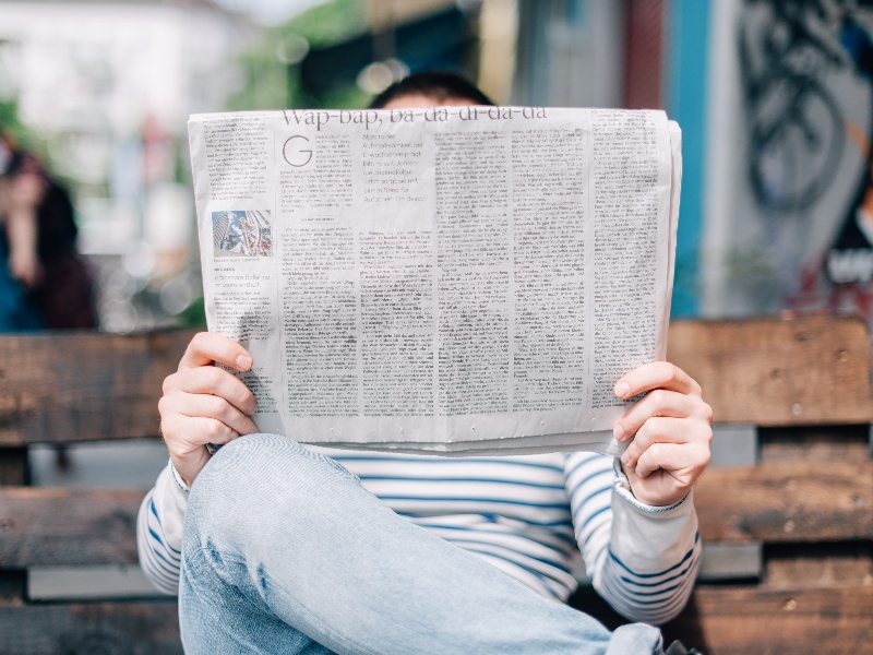 This is a lady sitting on a bench reading a newspaper