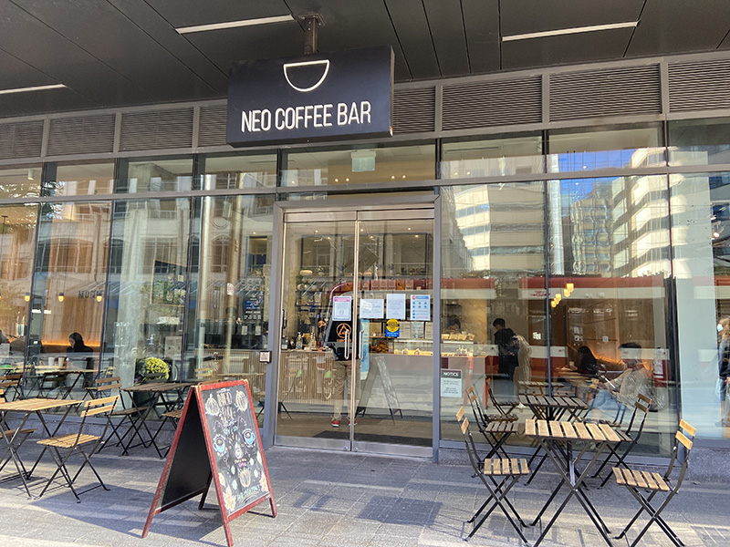 Neo Coffee Bar's glass windows and entrance are seen along with a few empty tables on the sidewalk