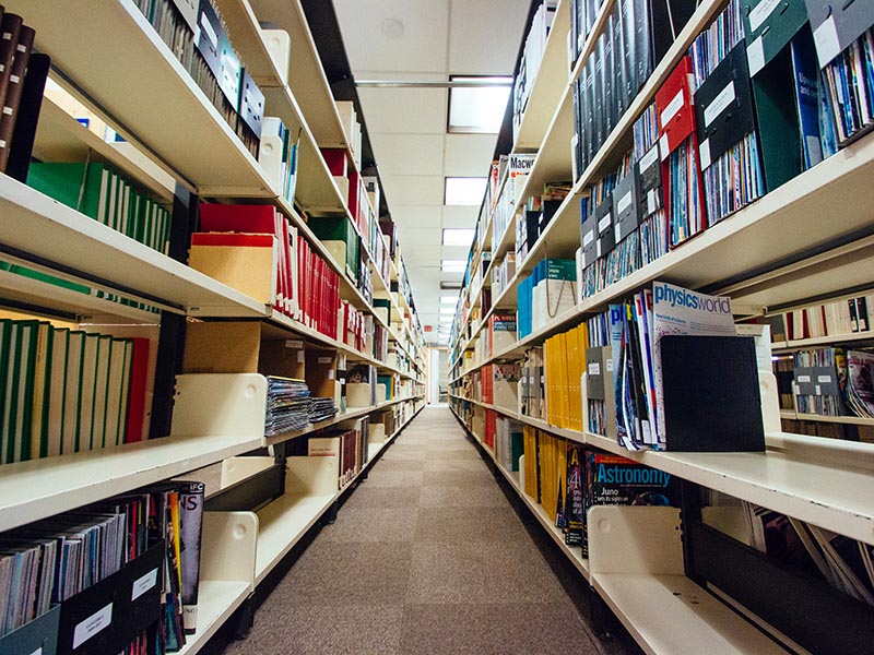 Two bookshelves are filled with books and magazines and seem to go on forever.