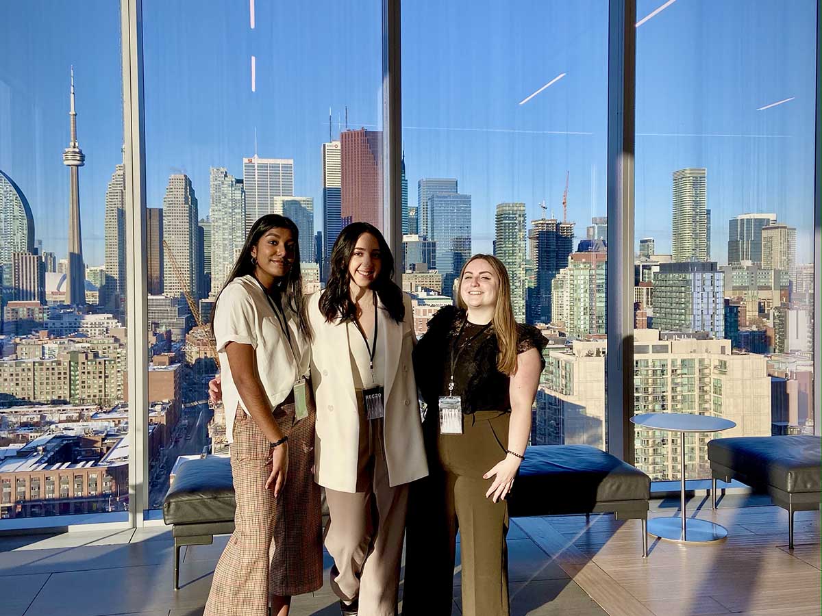 Three young women pose for a photo in front of the floor-to-ceiling windows in the Globe and Mail Centre.