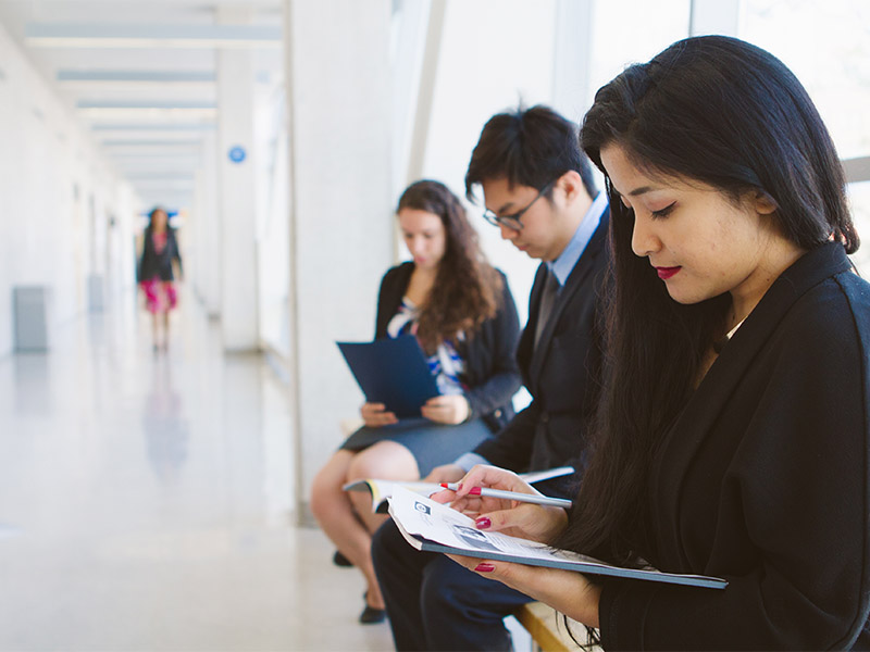 Three people dressed in business attire review their notes as they each wait to get interviewed