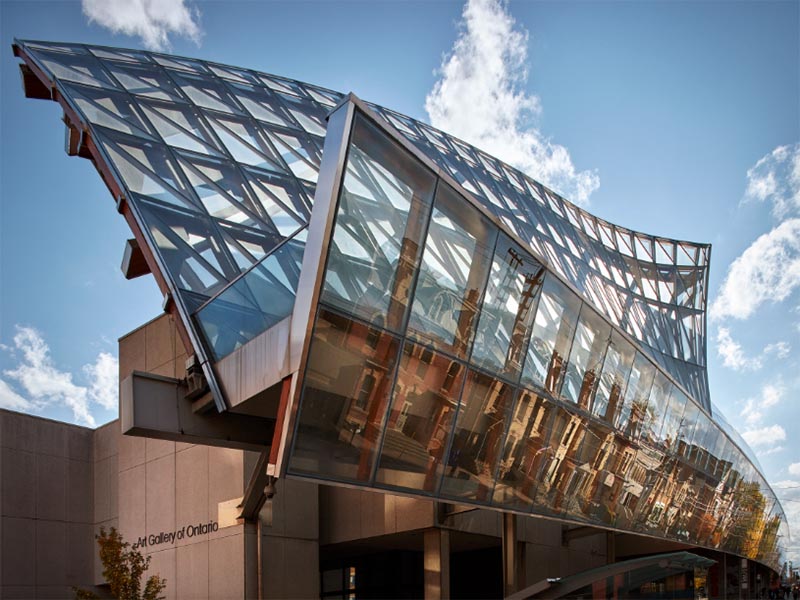 The warped glass top of the Art Gallery of Ontario sparkles against a bright blue cloudy sky.