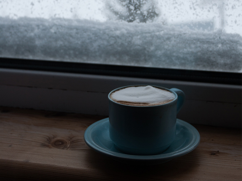 A cup of coffee sits on a snowy windowsill