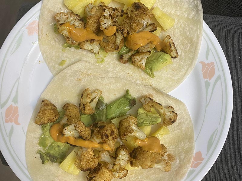 A plate of homemade cauliflower tacos with seasoned cauliflower, avocado, pineapple and chipotle sauce.