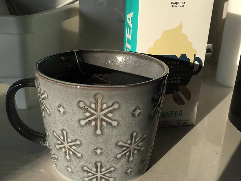 A large grey mug sits on a beige counter with a teabag inside it.
