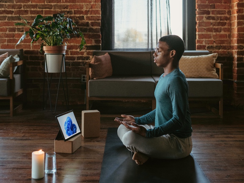 Person meditating on a yoga mat with a device and a candle
