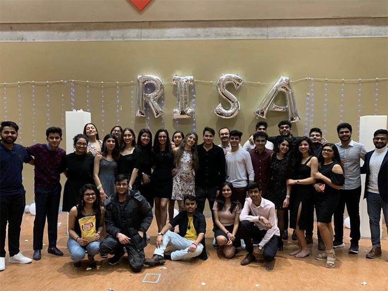 The Ryerson Indian Students Association stand in an event hall in front of silver balloons that spell out RISA after their Winter 2020 Semi-Formal