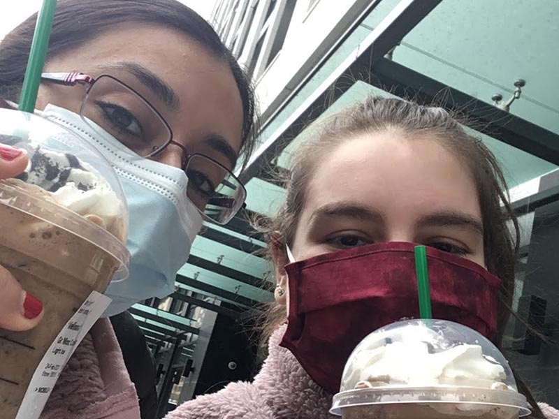 Jenna and Melissa hold Starbucks drinks while smiling under their masks.