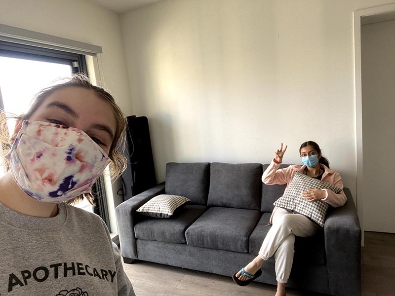 Jenna stands in her living room with Melissa sitting on their new couch. 