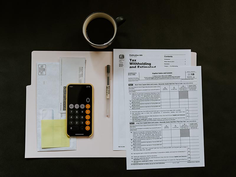 A birds-eye view of a cup of coffee, folder, calculator and tax forms on a dark table. 