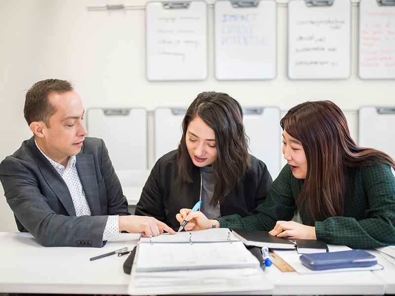 Two instructors sit down with a student and assist her with her work