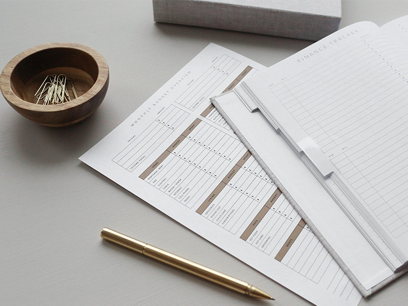 A monthly budget overview sheet and a finance tracker book are laid out on a table