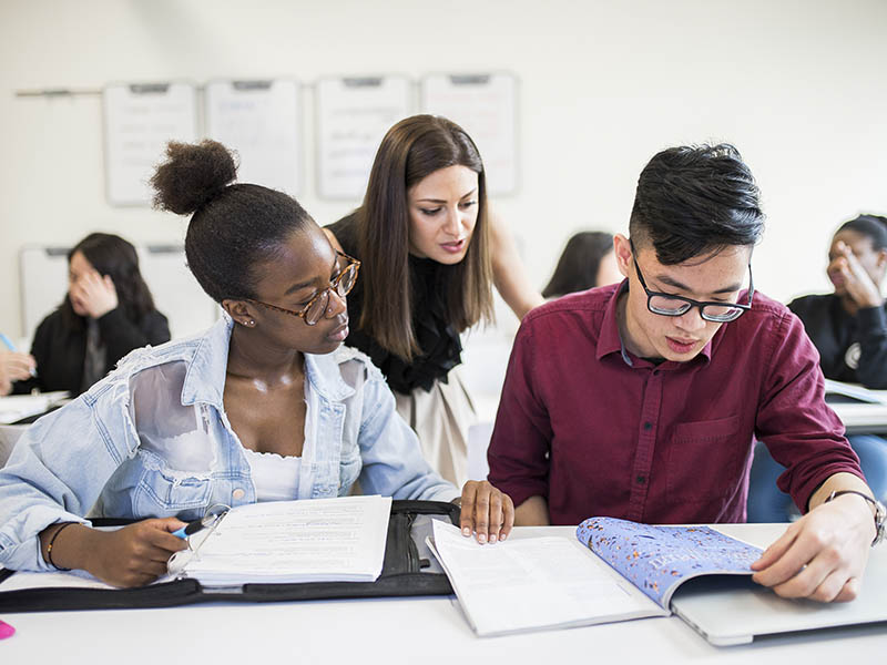 A teacher assists two students with their schoolwork while they look through their notes.