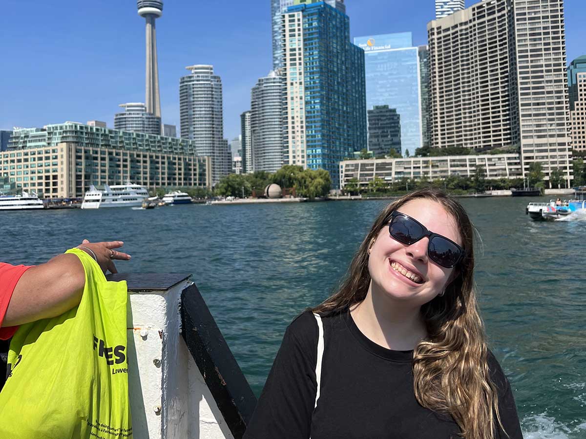 Jenna smiles while on the Toronto Islands ferry with the Toronto skyline in the background.
