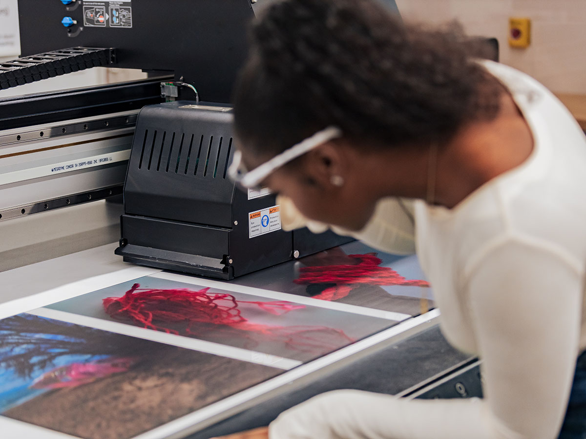 A student wearing protective goggles works with photographs in a creative lab.  