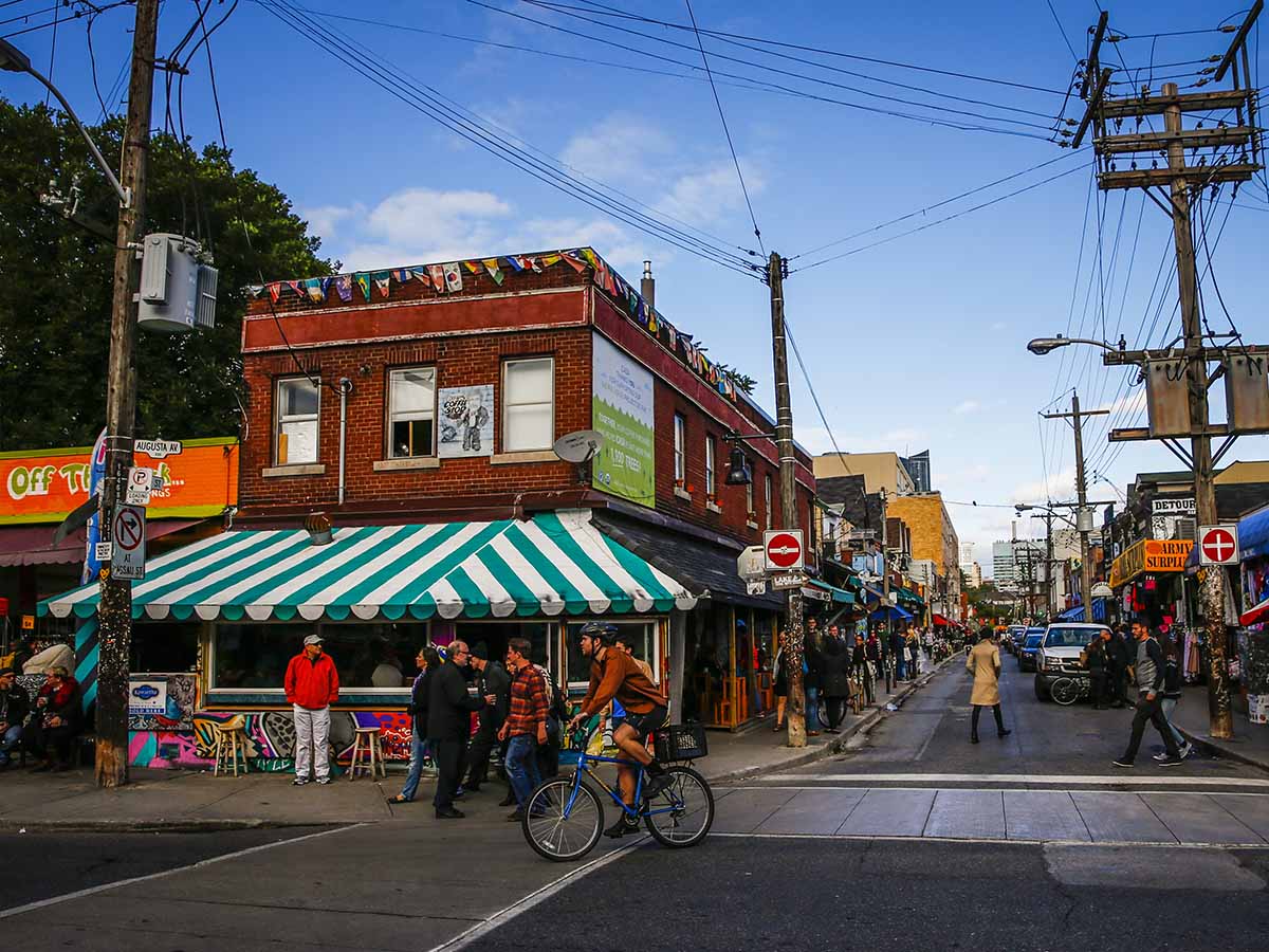 Pedestrians explore Kensington Market's bright and unique storefronts on a sunny, fall day.