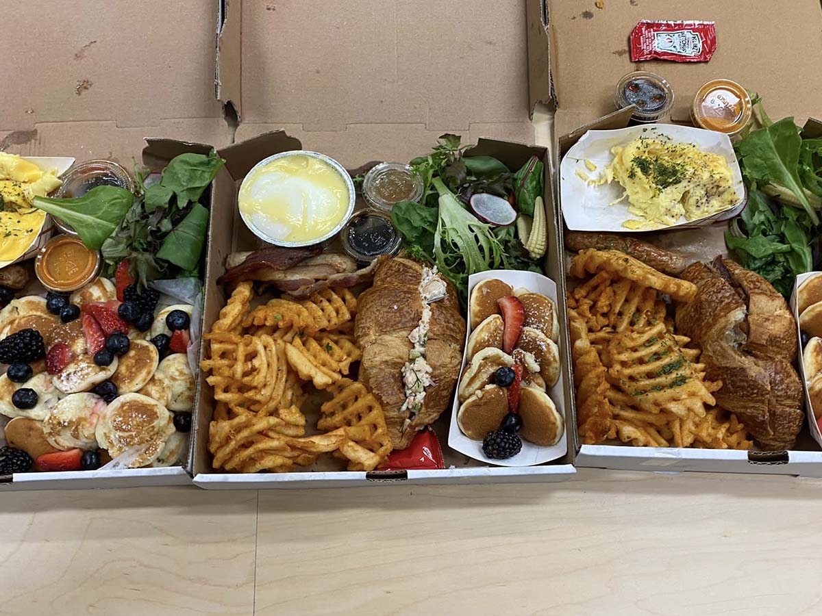 Three brunch boxes filled with waffle fries, pancakes, pastries and more. 