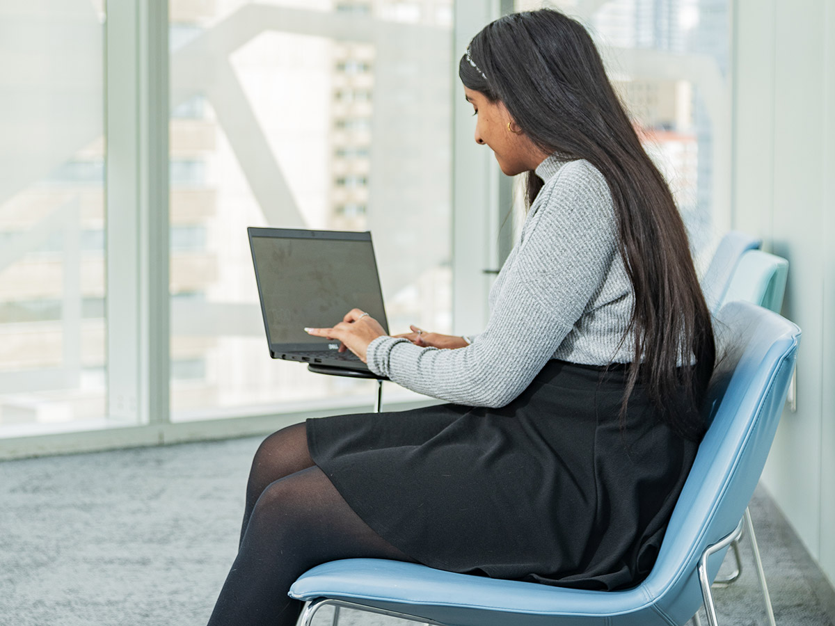 A student sits and works on her laptop in front of a window on the eighth floor of the Student Learning Centre.