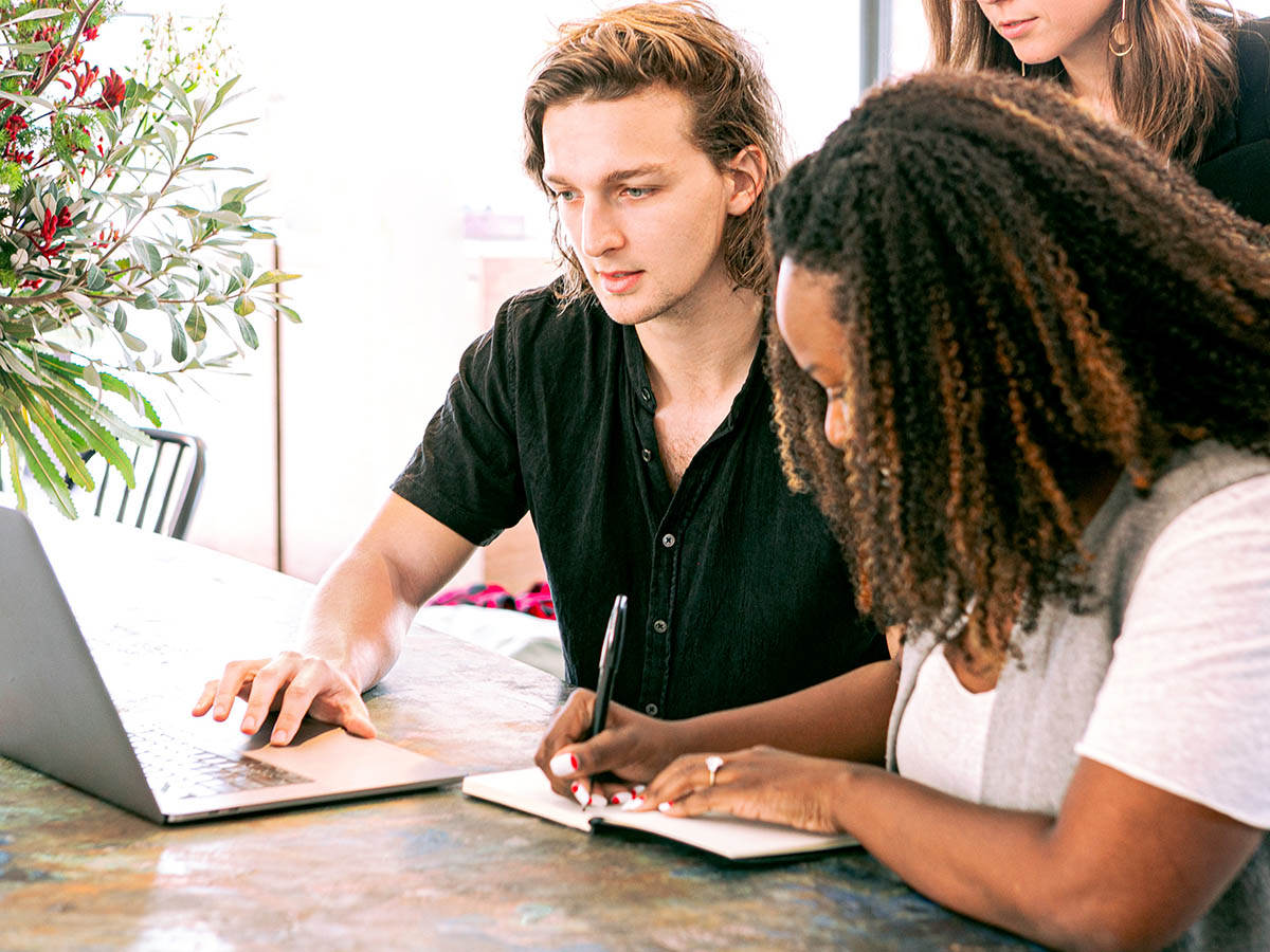 Students gather around a laptop while one takes notes.