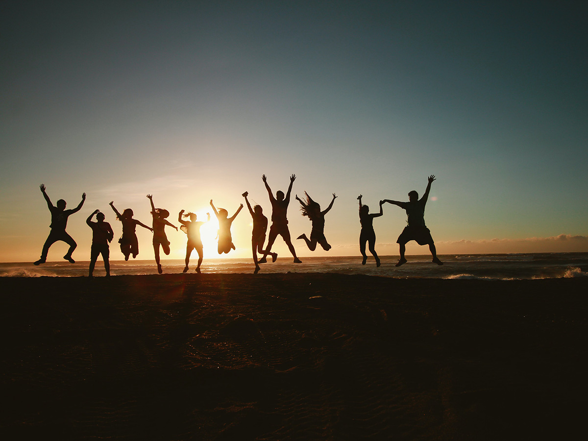 A group of friends taking a photo of them jumping in front of a sunset.