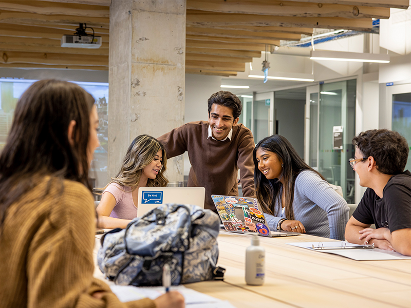 A group of students laugh as they look at a laptop screen together.