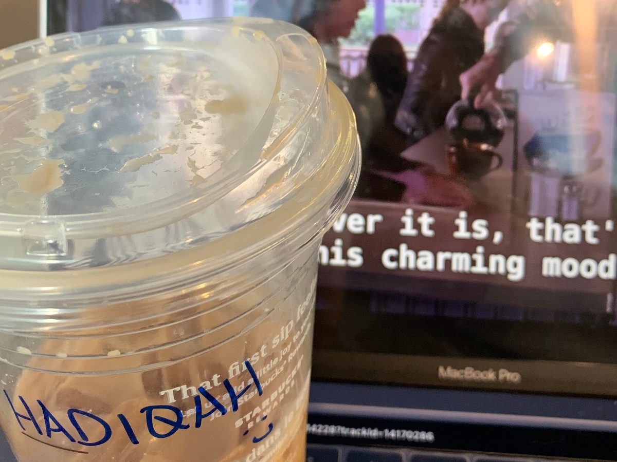Coffee with "Hadiqah" written on the cup in front of a laptop screen.